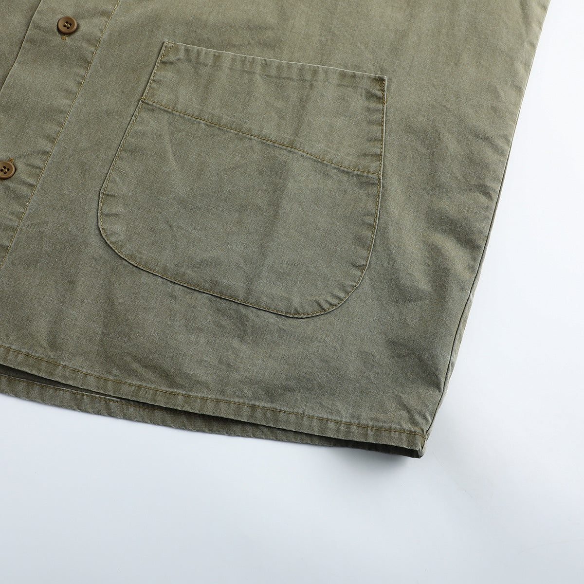 Close-up of a large rounded patch pocket and button placket on an olive-gray shirt.