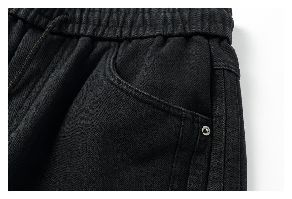 Close-up of black trousers showing the elastic waistband, drawstring, curved pocket and metal rivet.