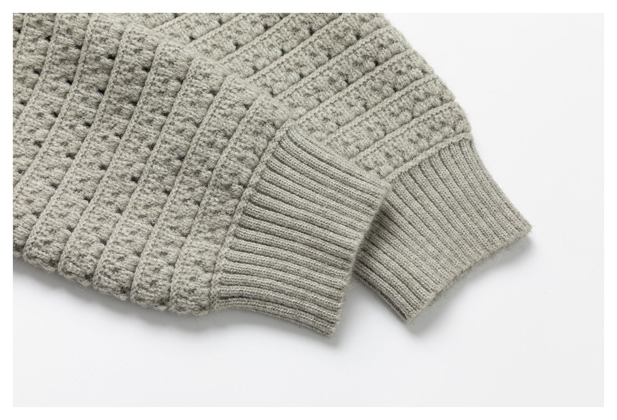 Close-up of a light gray knit sweater sleeve with a ribbed cuff beside the textured body.