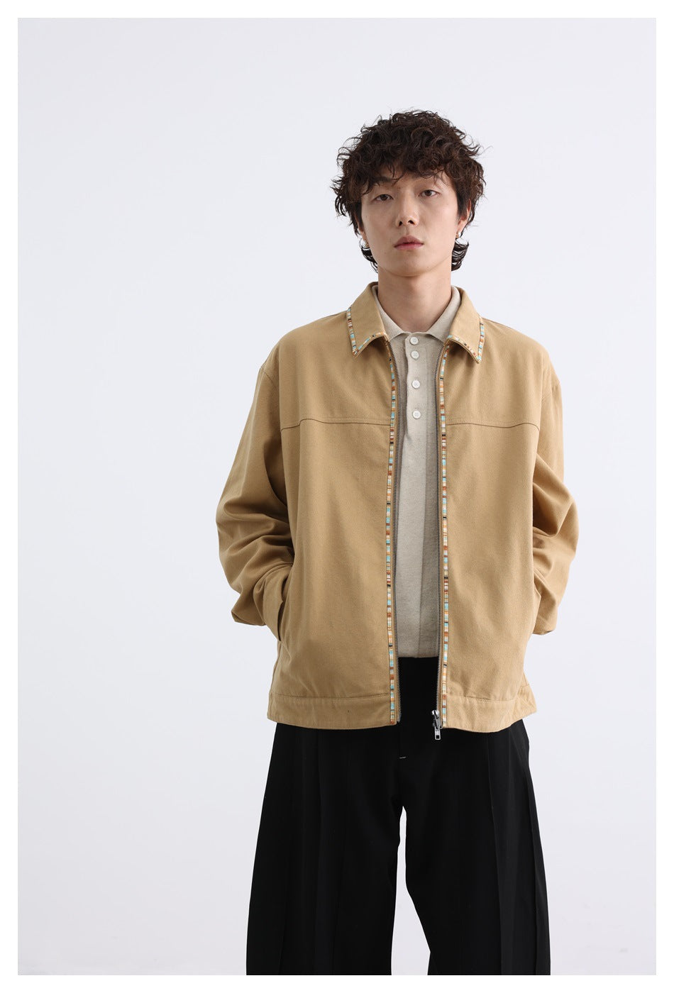 Front view of a model in a tan zip-front jacket with multicolor trim, a beige shirt, and black trousers.