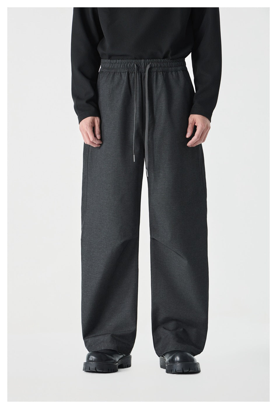 Front view of a model wearing charcoal wide-leg pants with an elastic drawstring waist and black shoes.