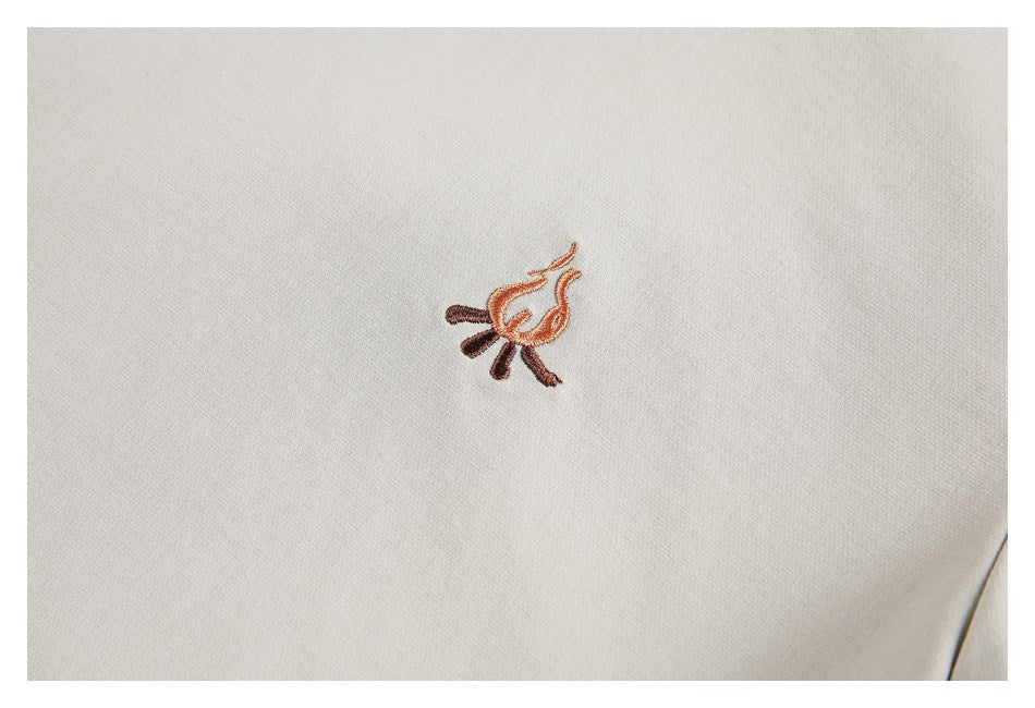 Close-up of a small orange and brown embroidered flame-like motif on beige fabric.