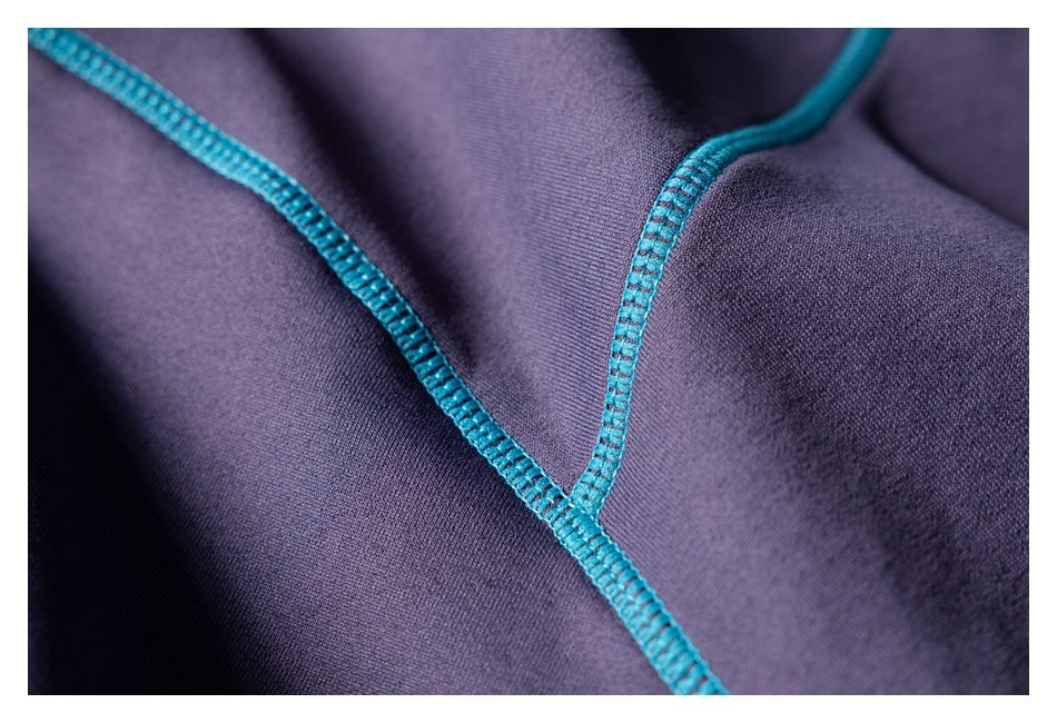 Close-up of bright teal overlock stitching crossing dark purple garment fabric.
