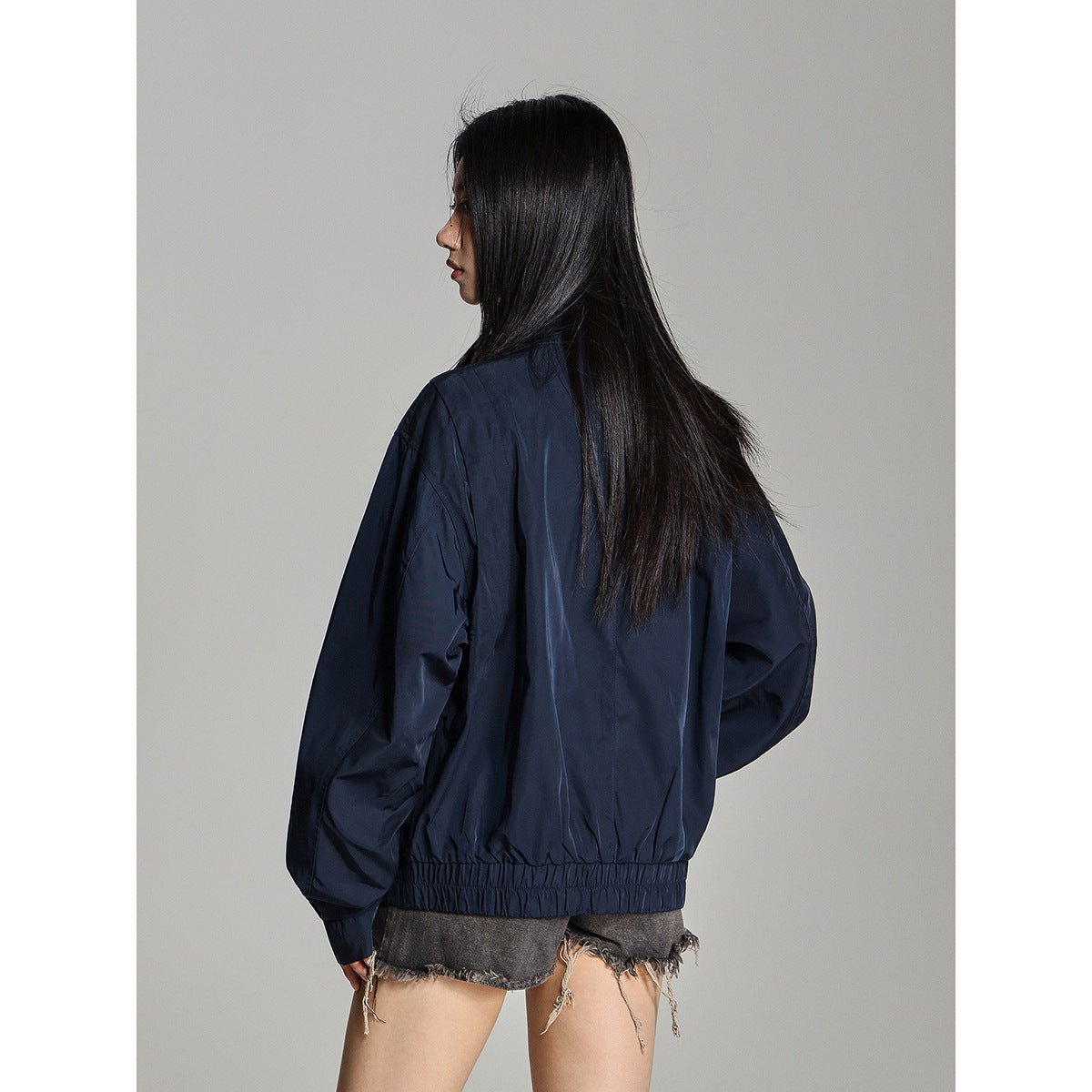 Rear view of a model wearing a navy jacket with a gathered elastic hem.
