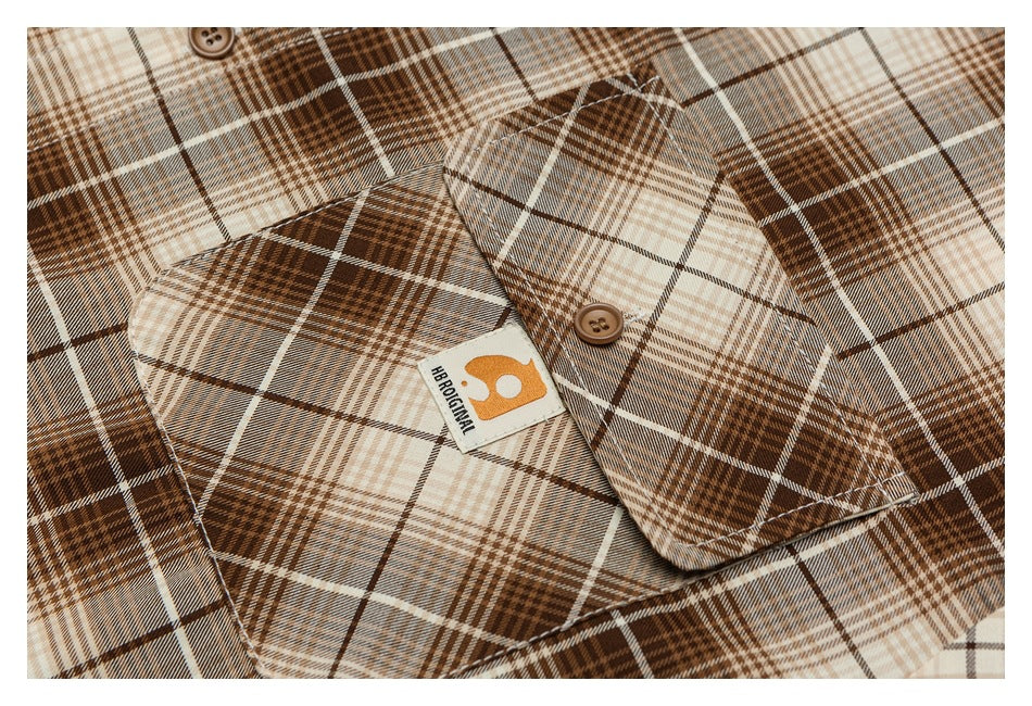 Close-up of a brown, cream, and gray plaid shirt pocket, button, and sewn label.