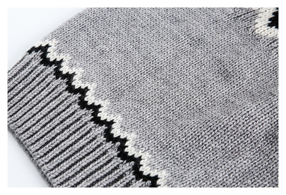 Close-up of a gray knit sweater sleeve edge with ribbed cuff and a black-and-cream zigzag stripe.