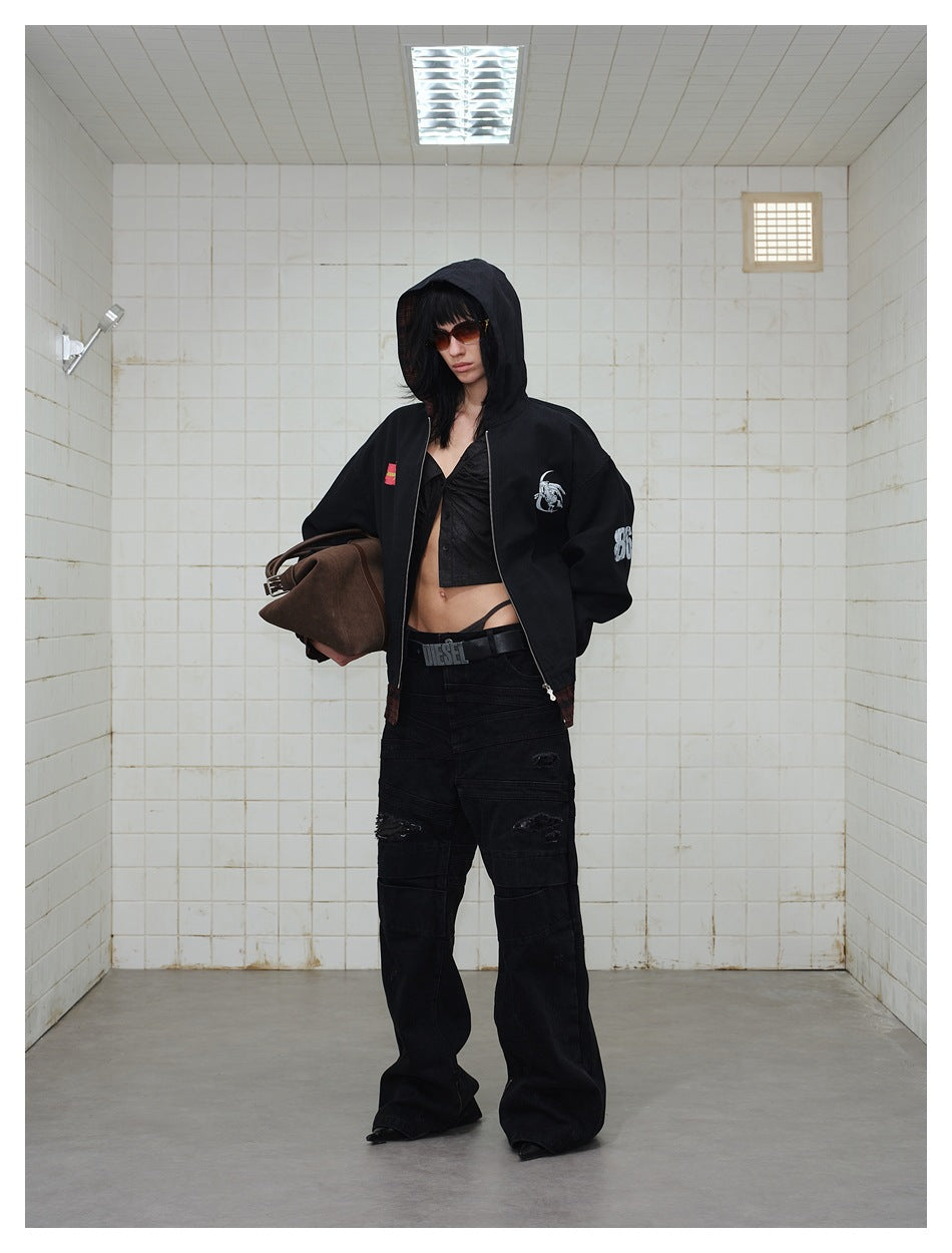 Model wearing a black zip-front hooded jacket with graphic patches and burgundy plaid trim, paired with black pants.