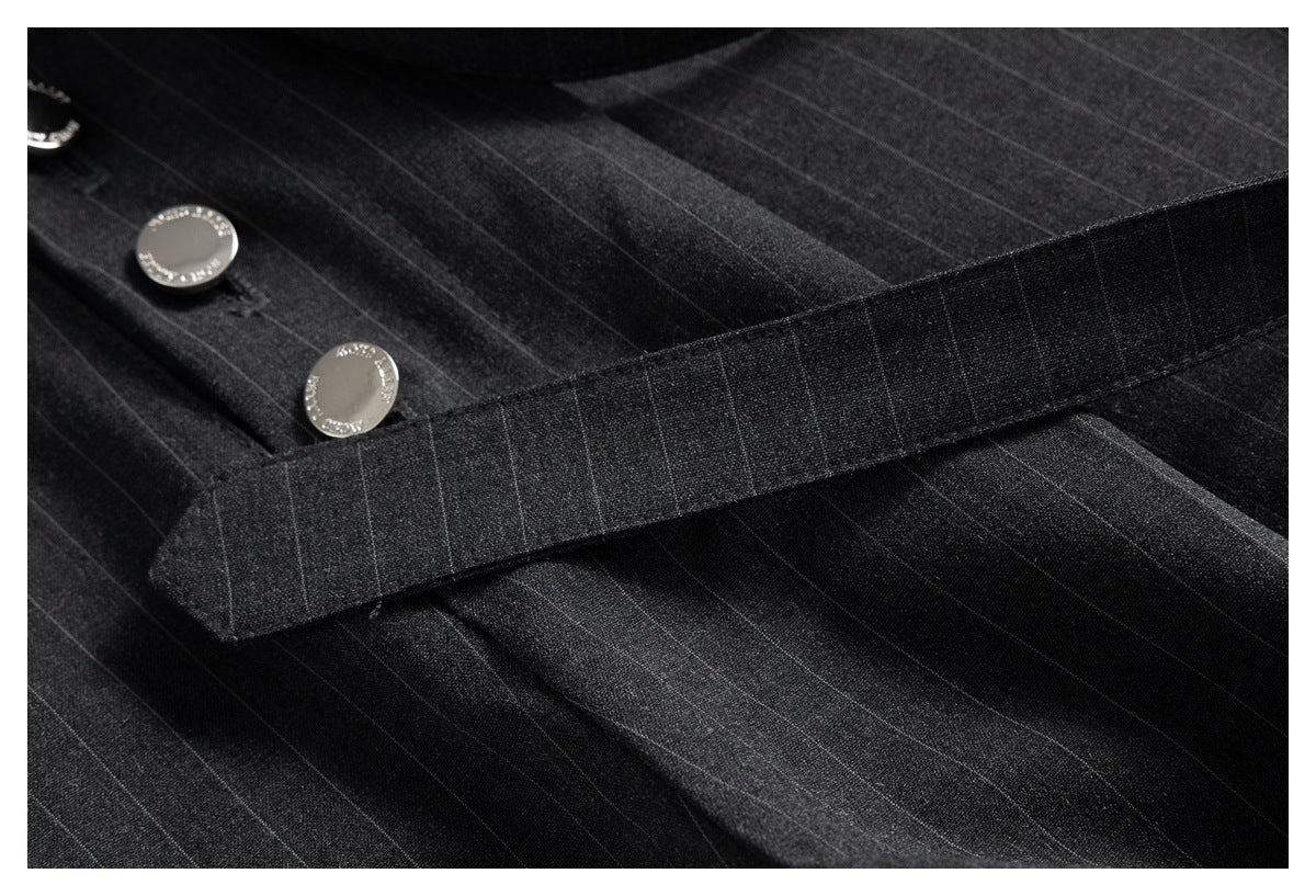 Close-up of dark pinstripe trousers with a matching fabric strap and round silver buttons.