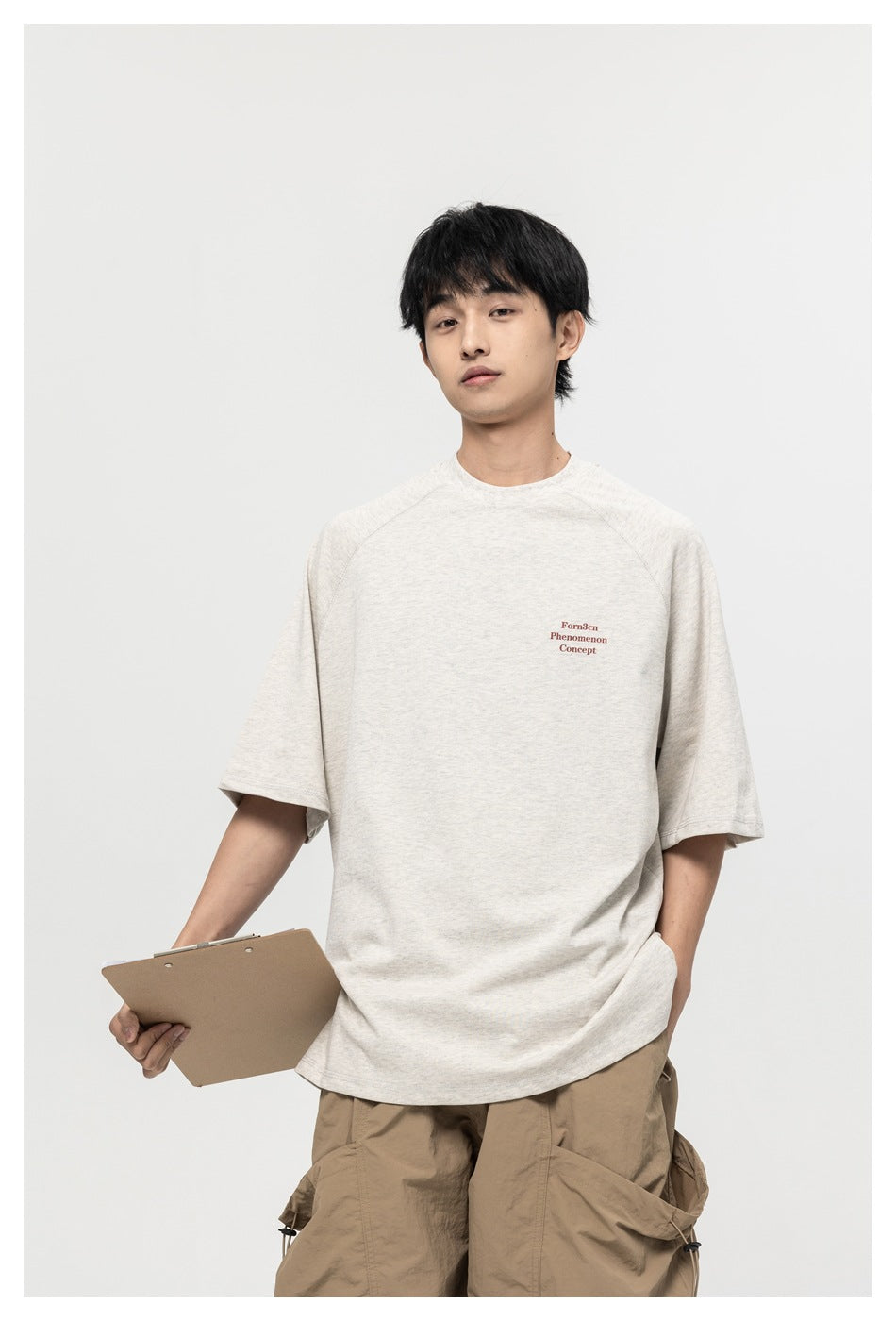Model wearing an oversized off-white raglan T-shirt with small burgundy chest text and tan cargo pants.
