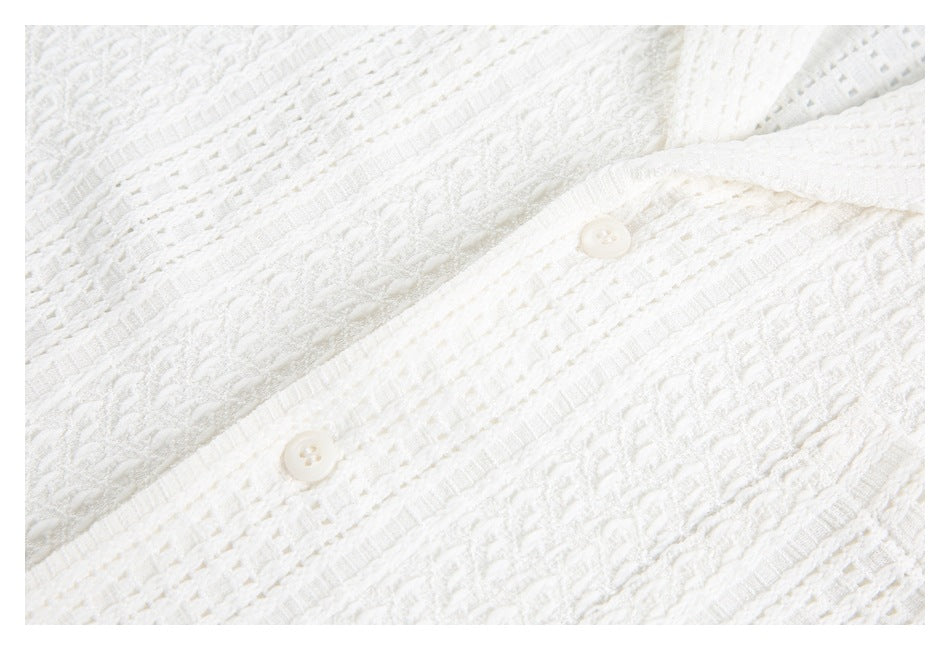Close-up of two white buttons and the raised openwork texture on a white tunic.