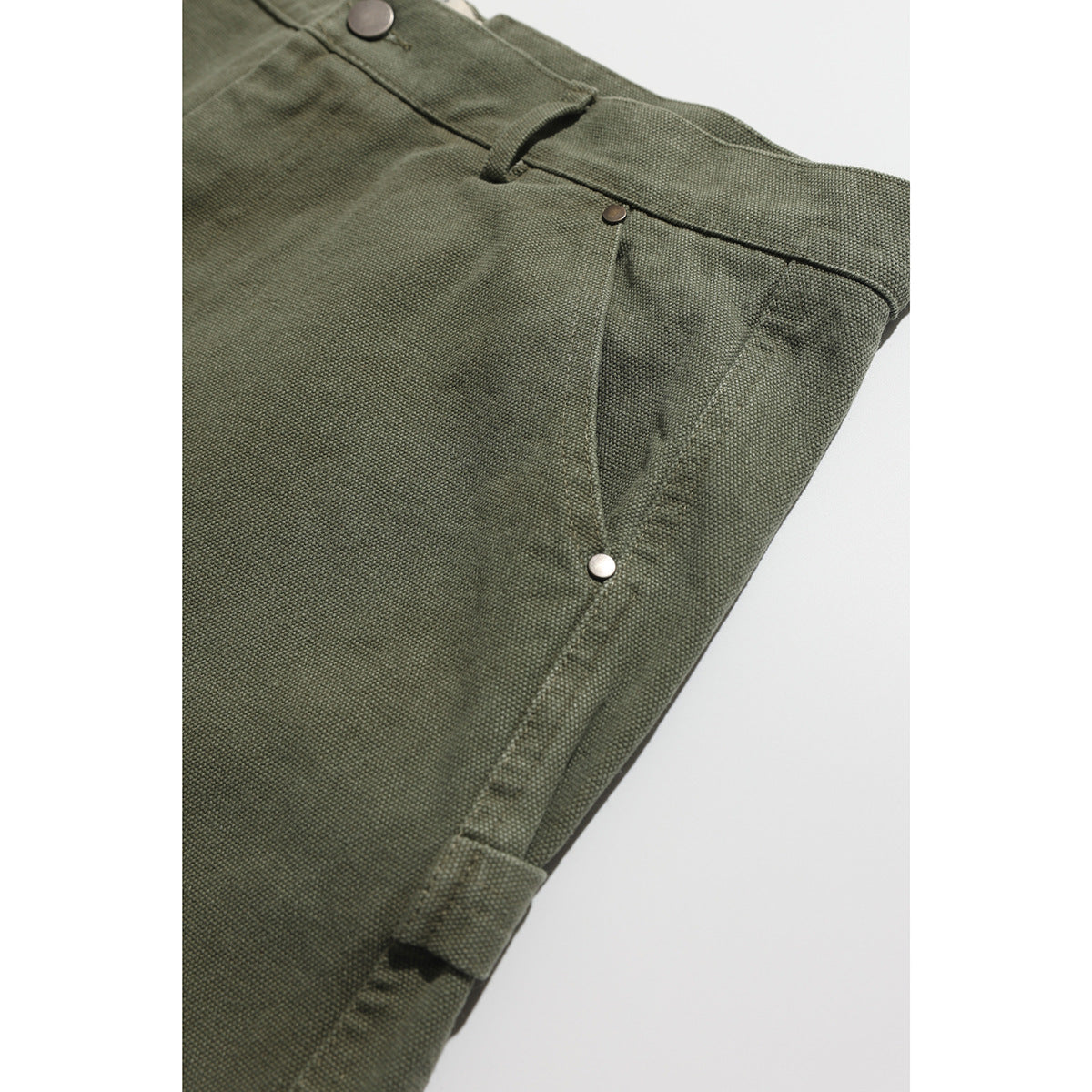 Close-up of olive shorts showing the waistband, front pocket rivet, side seam, and hem tab.
