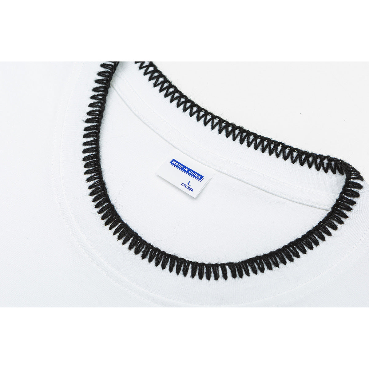 Close-up of a white T-shirt neckline with black blanket stitching and a sewn size label.