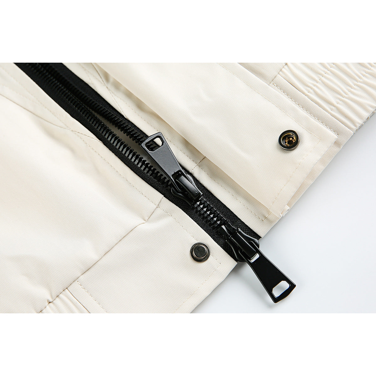 Close-up of a cream jacket's black front zipper, metal snaps, and stitched placket.