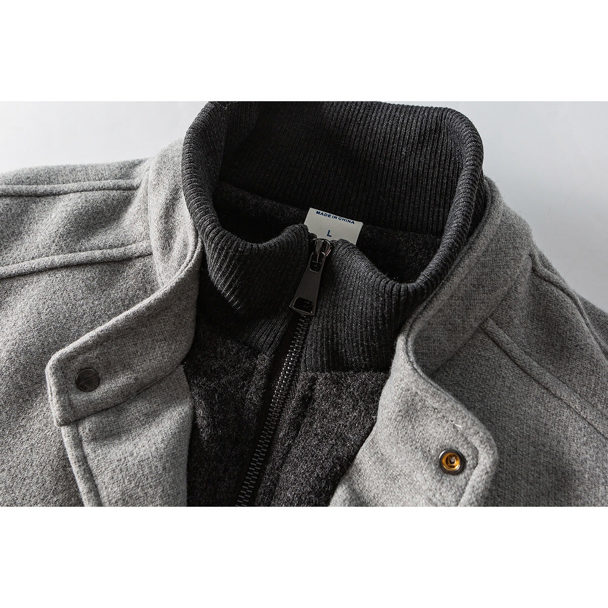 Close-up of a gray jacket with a dark ribbed stand collar, front zipper and snap-fastened flap.