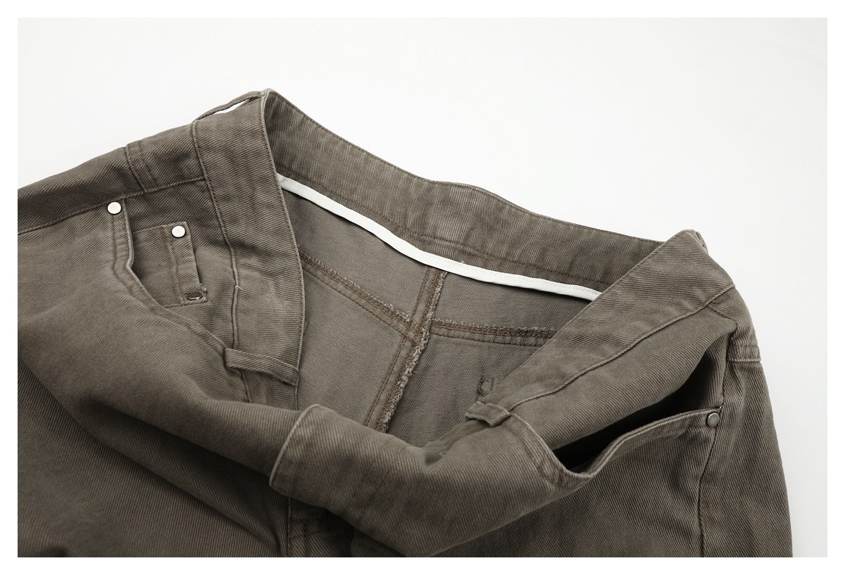 Close-up of taupe-gray trousers at the front waist, showing the open waistband, button closure, and inner seams.