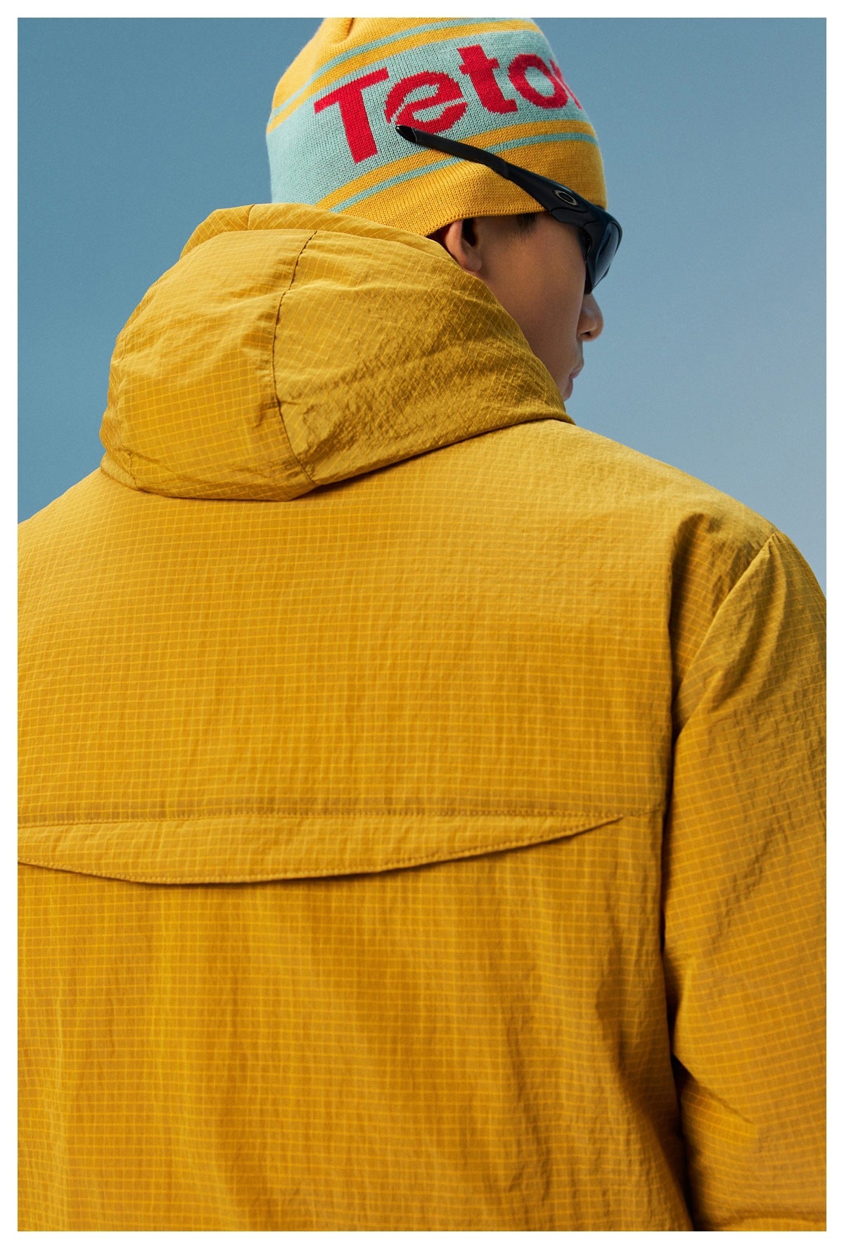 Close rear view of a mustard grid-pattern hooded pullover, showing the hood and back panel.