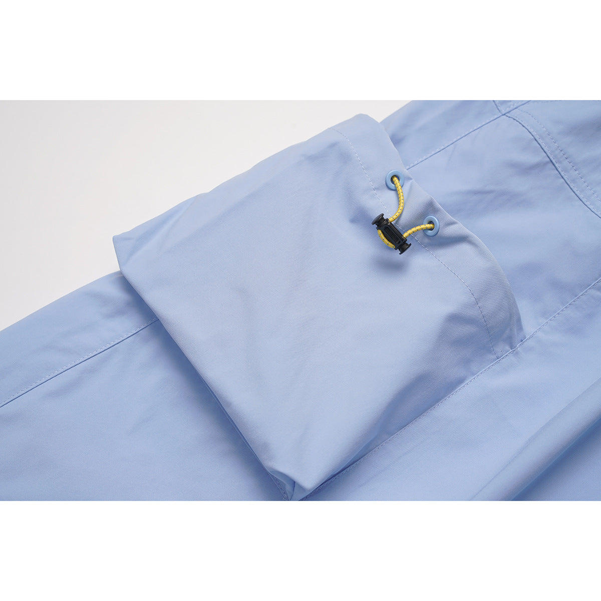 Close-up of a light blue skirt's flap pocket with a yellow cord toggle.