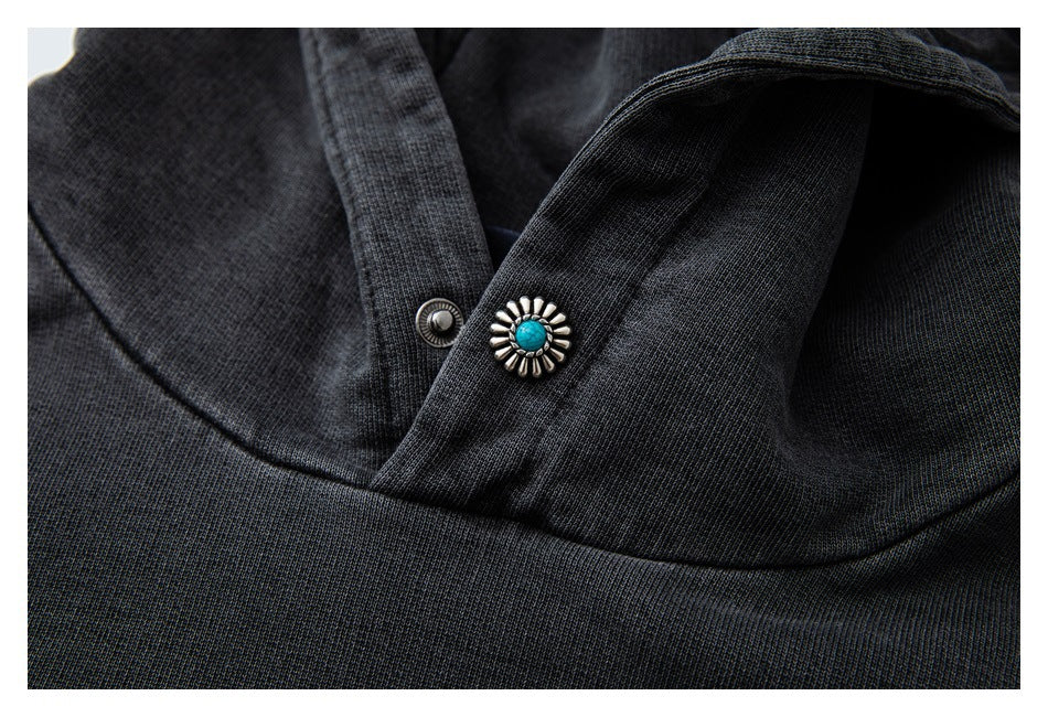 Close-up of a charcoal hoodie neckline with a metal snap and a turquoise-centered floral decorative button.