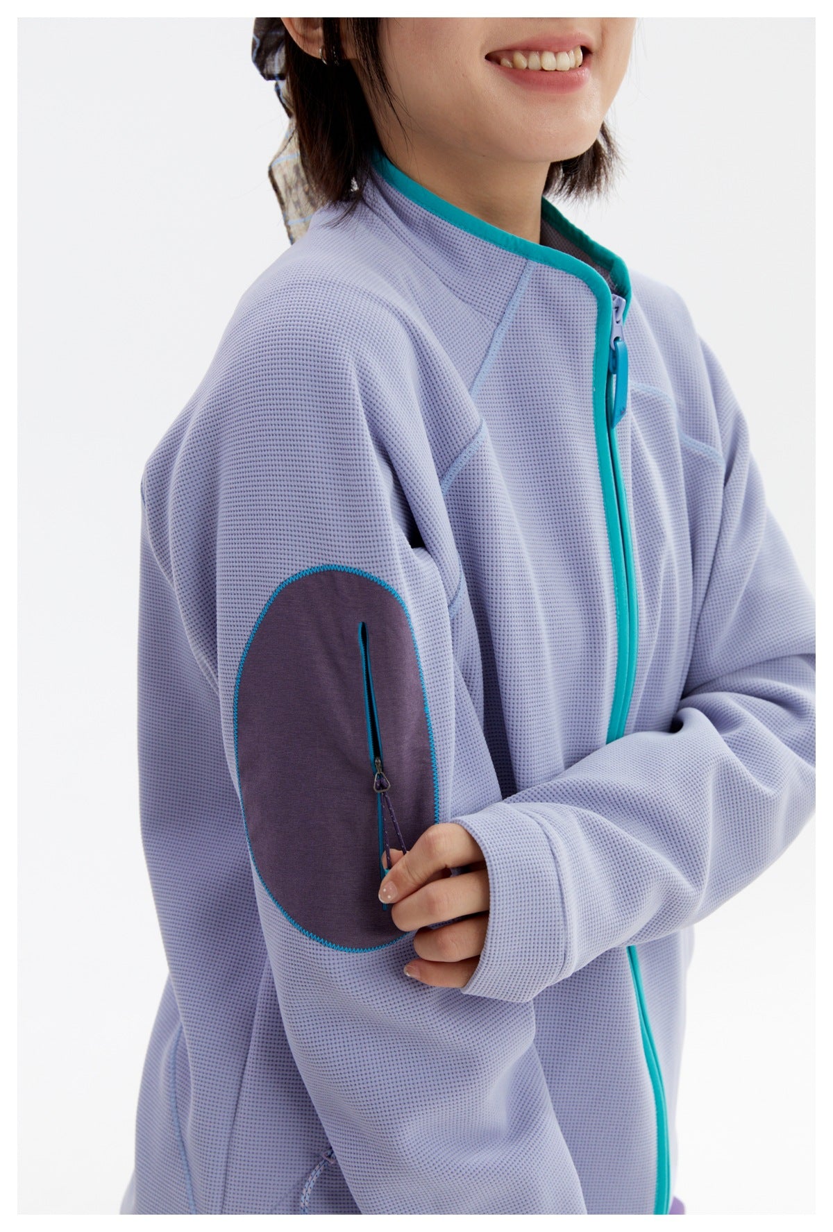 Close-up of the lavender jacket’s dark elbow patch, teal stitching and vertical zip pocket.