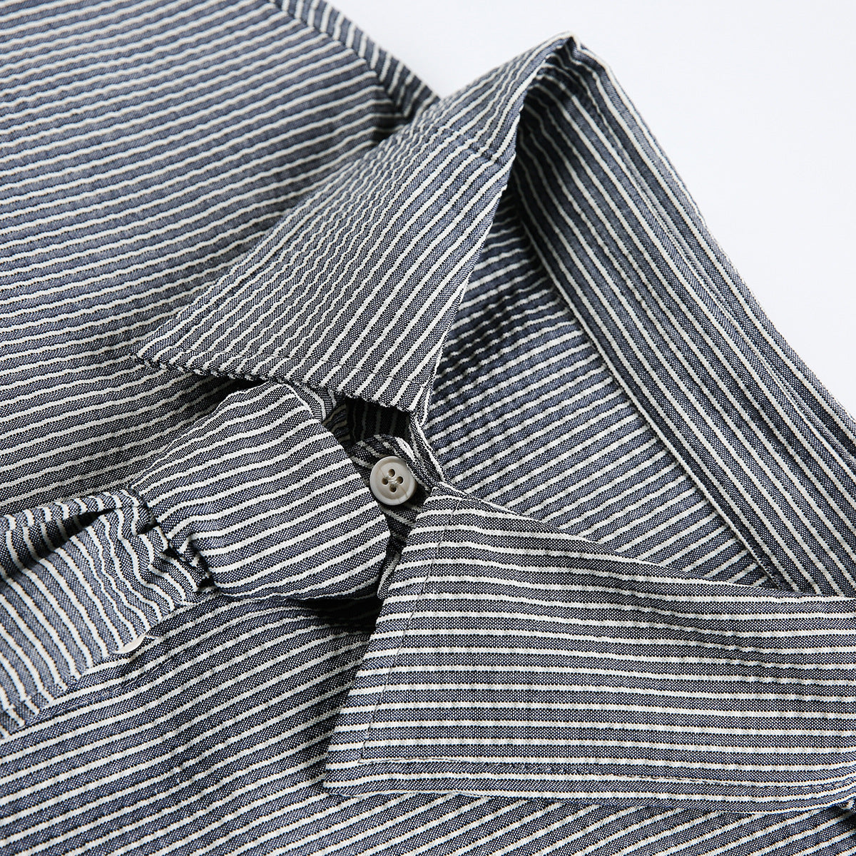 Close-up of a pointed collar and button on a dark shirt with narrow light stripes.