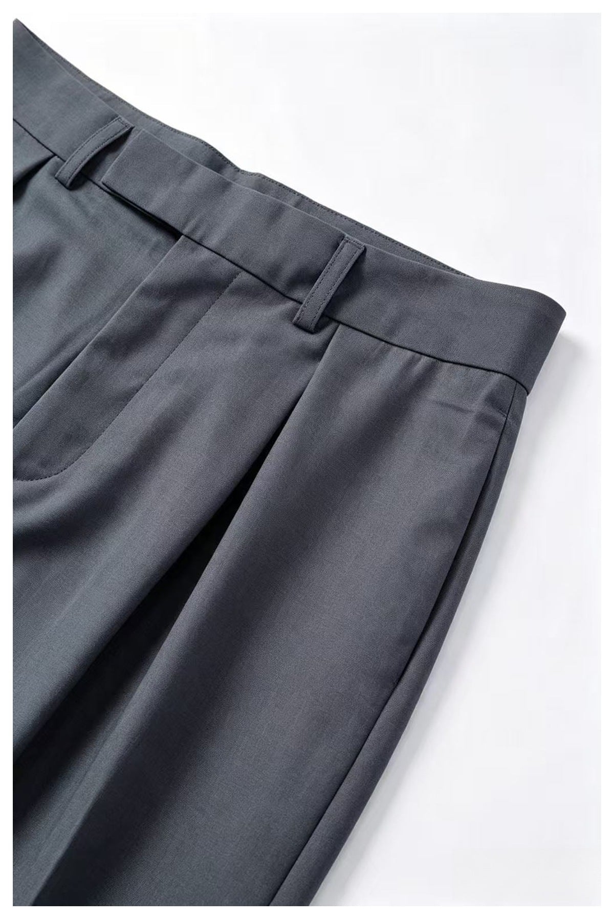 Close-up of charcoal-gray trousers showing the front waistband, belt loops, and pleated front.