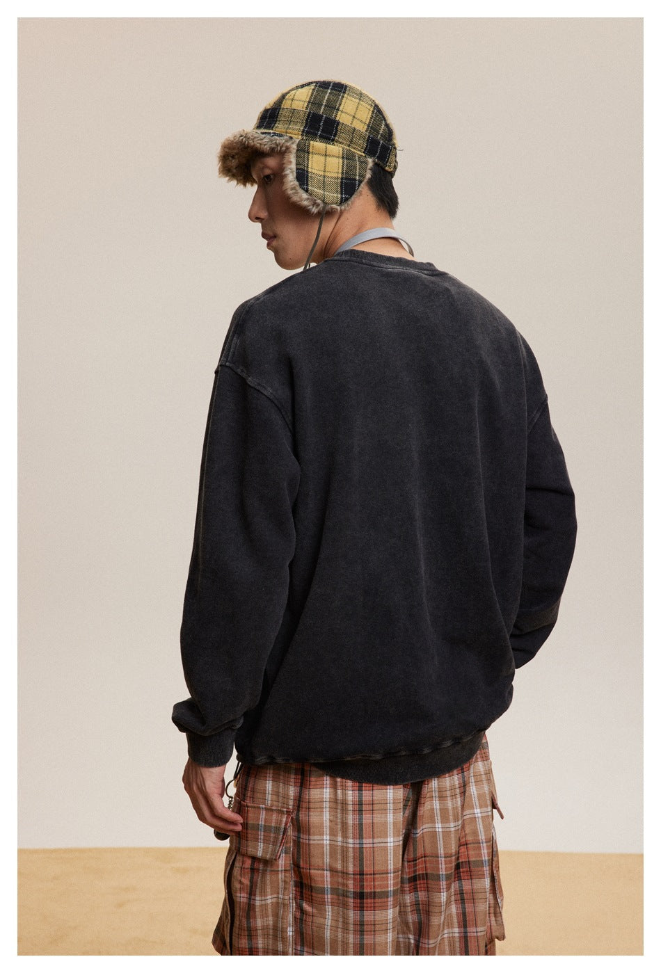Back view of a model wearing a charcoal crewneck sweatshirt and plaid trousers.