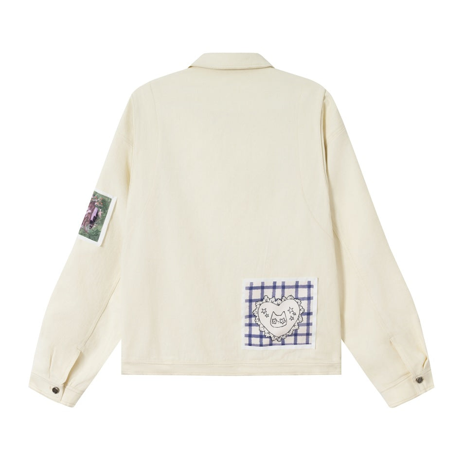 Back of an ivory jacket with a blue checked heart patch near the hem and an illustrated sleeve patch.