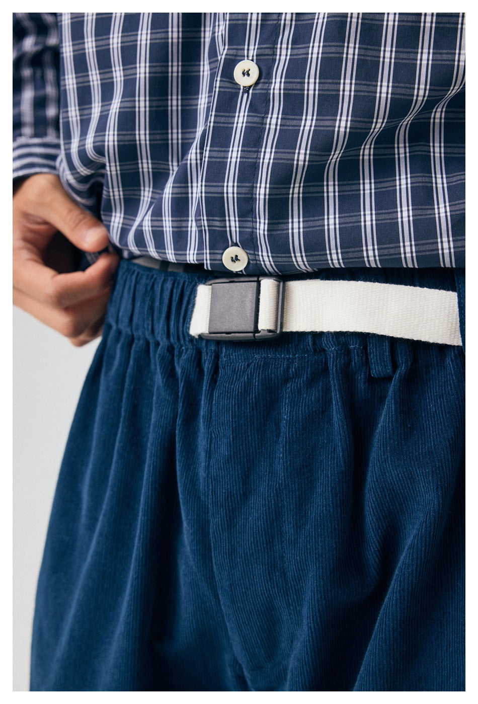 Close-up of a white belt at the waist of navy pants beneath a blue plaid shirt.