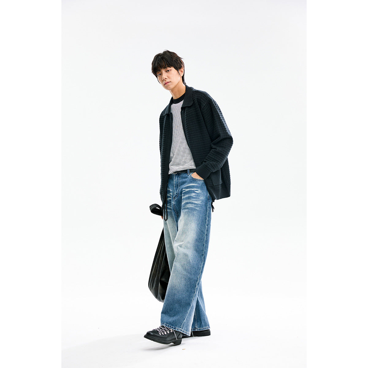 Model wearing a black textured collared cardigan over a striped shirt with loose blue jeans.