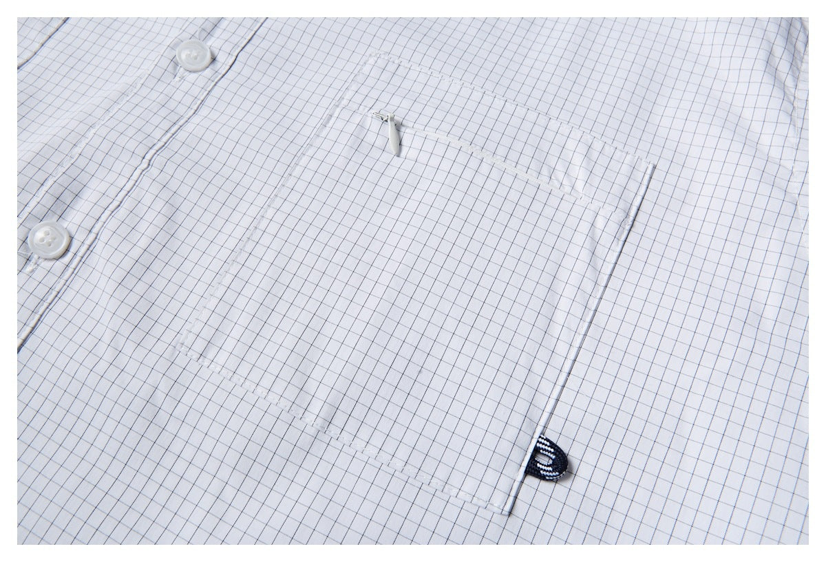 Close-up of the white grid-check shirt's large chest pocket, with a small zipper and white buttons nearby.