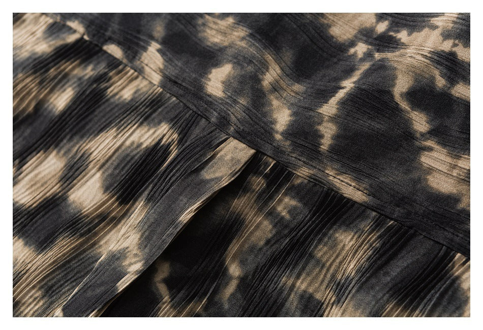 Close-up of overlapping pleated panels on a dark garment with a beige abstract pattern.