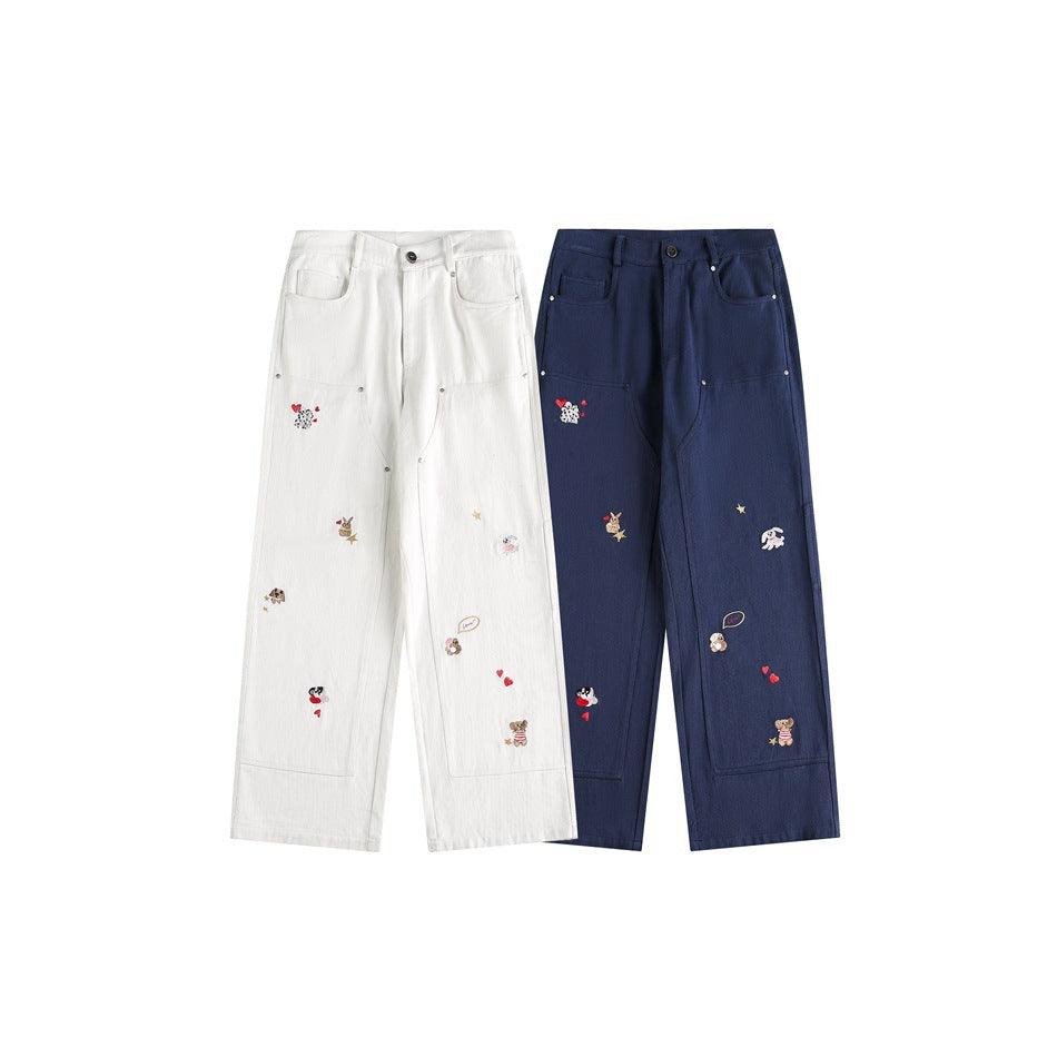 Two wide-leg pants shown from the front in ivory and navy, each with utility pockets and scattered embroidered motifs.