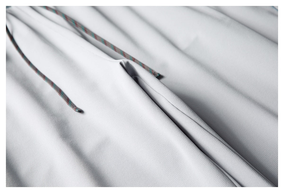 Close-up of light gray fabric with patterned drawstrings and a folded seam.