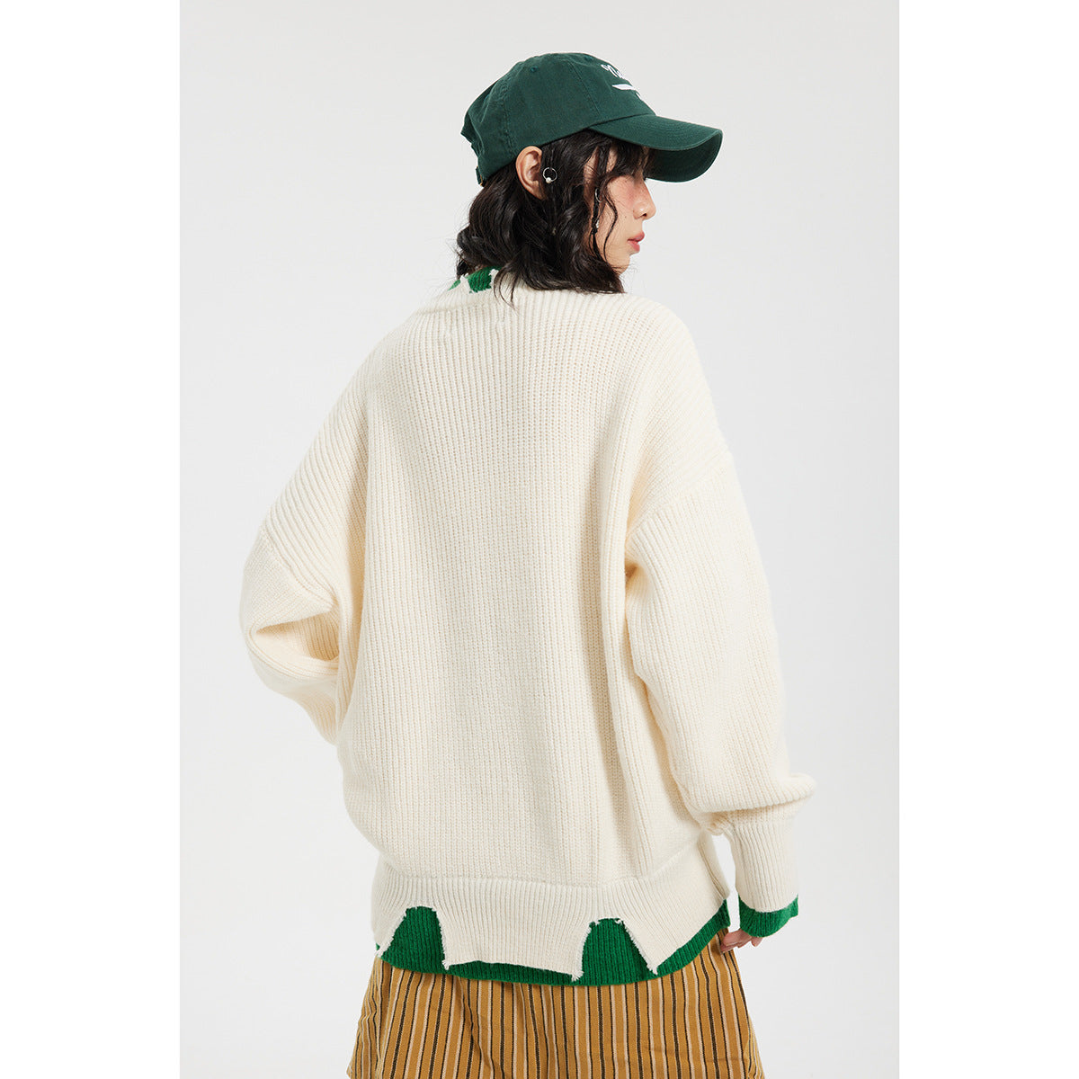 Rear view of a model wearing the ivory sweater with green trim and a scalloped color-block hem.