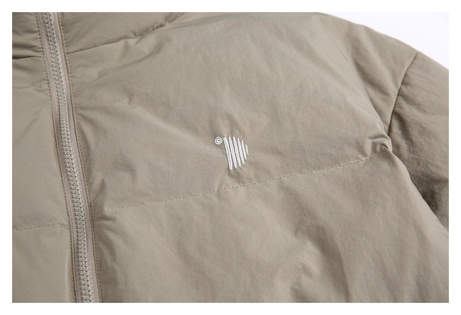 Close-up of a small white embroidered mark on the taupe jacket's chest beside the zipper.