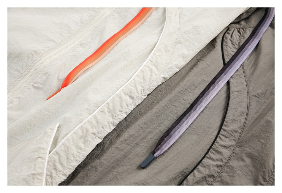 Close-up of cream and taupe jacket fabric with contrasting orange and lavender drawstrings.