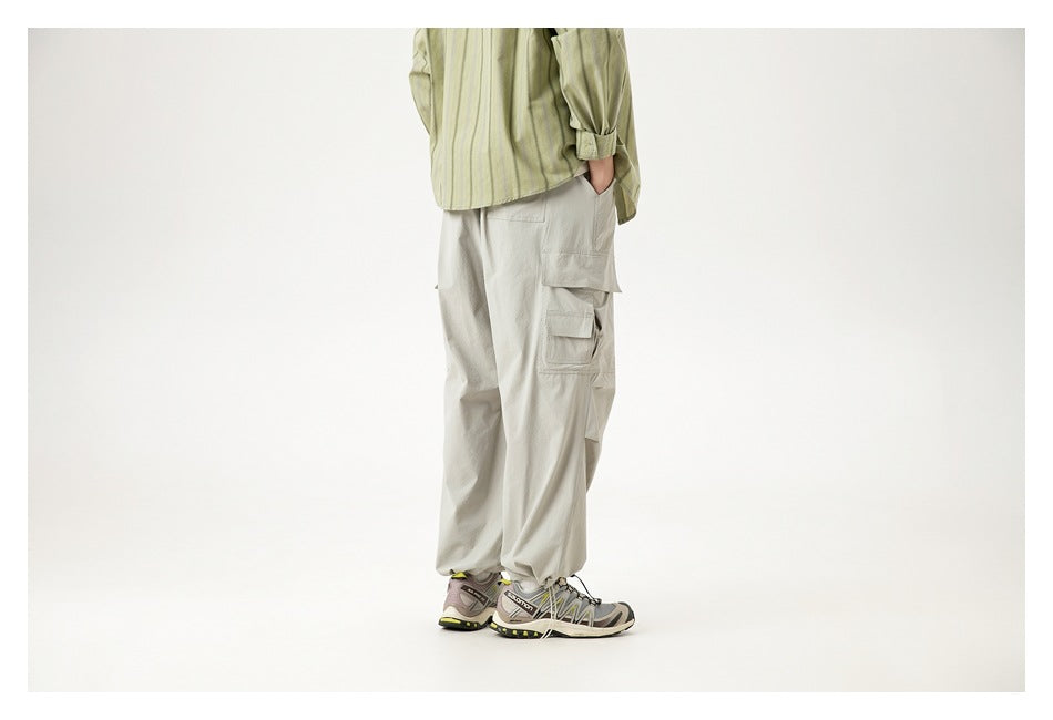 Rear three-quarter view of a cropped model wearing loose light gray cargo pants with flap pockets.