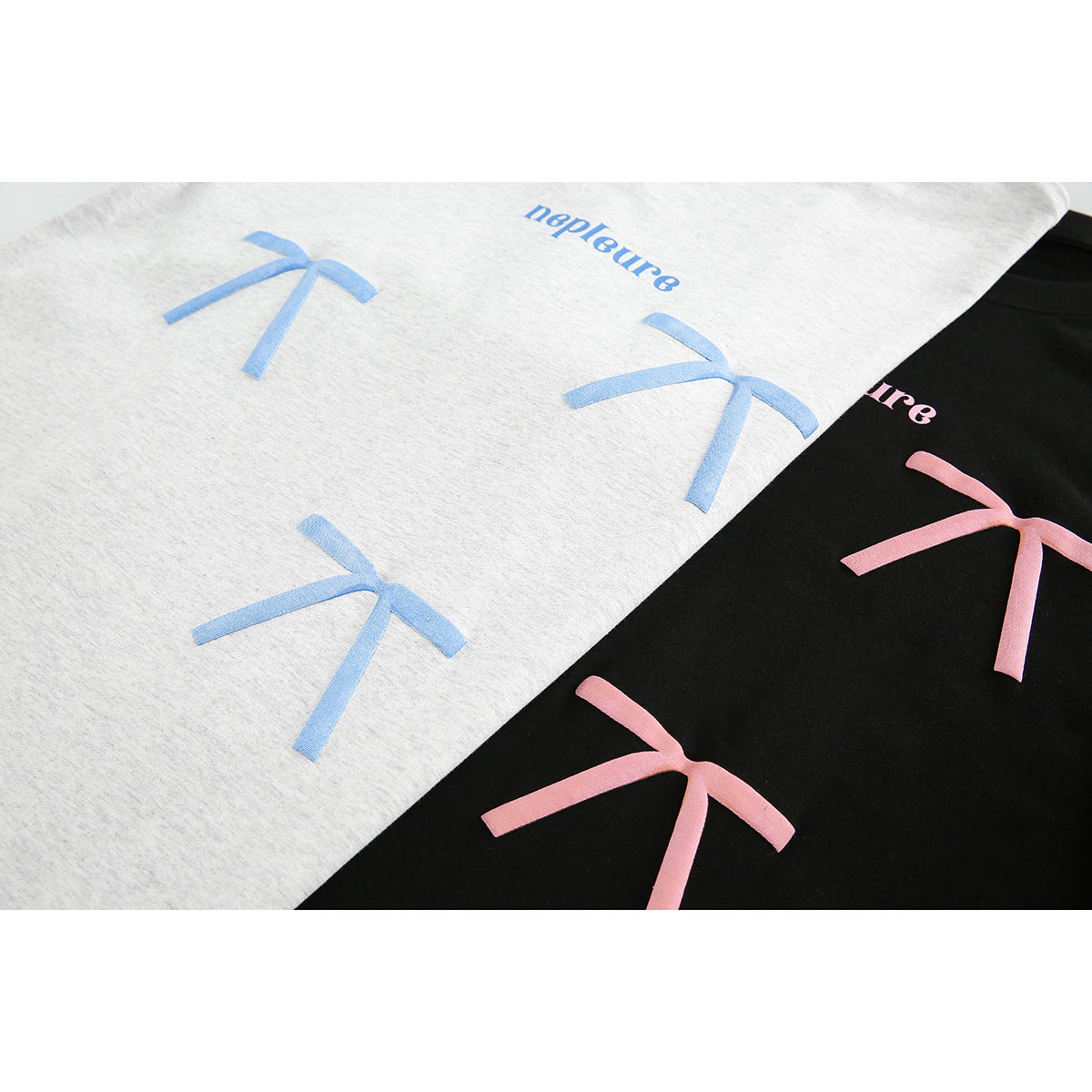Close-up of light gray and black T-shirts with large blue and pink bow prints and small wordmarks.