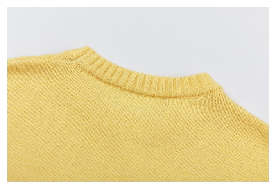 Close-up of a pale yellow knitted sweater showing its ribbed crew neckline and shoulder.