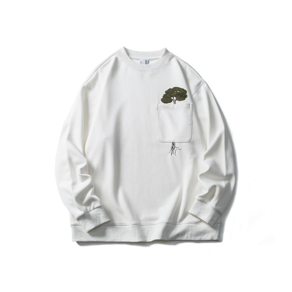 White crewneck sweatshirt flat lay with chest pocket and green embroidered tree with roots