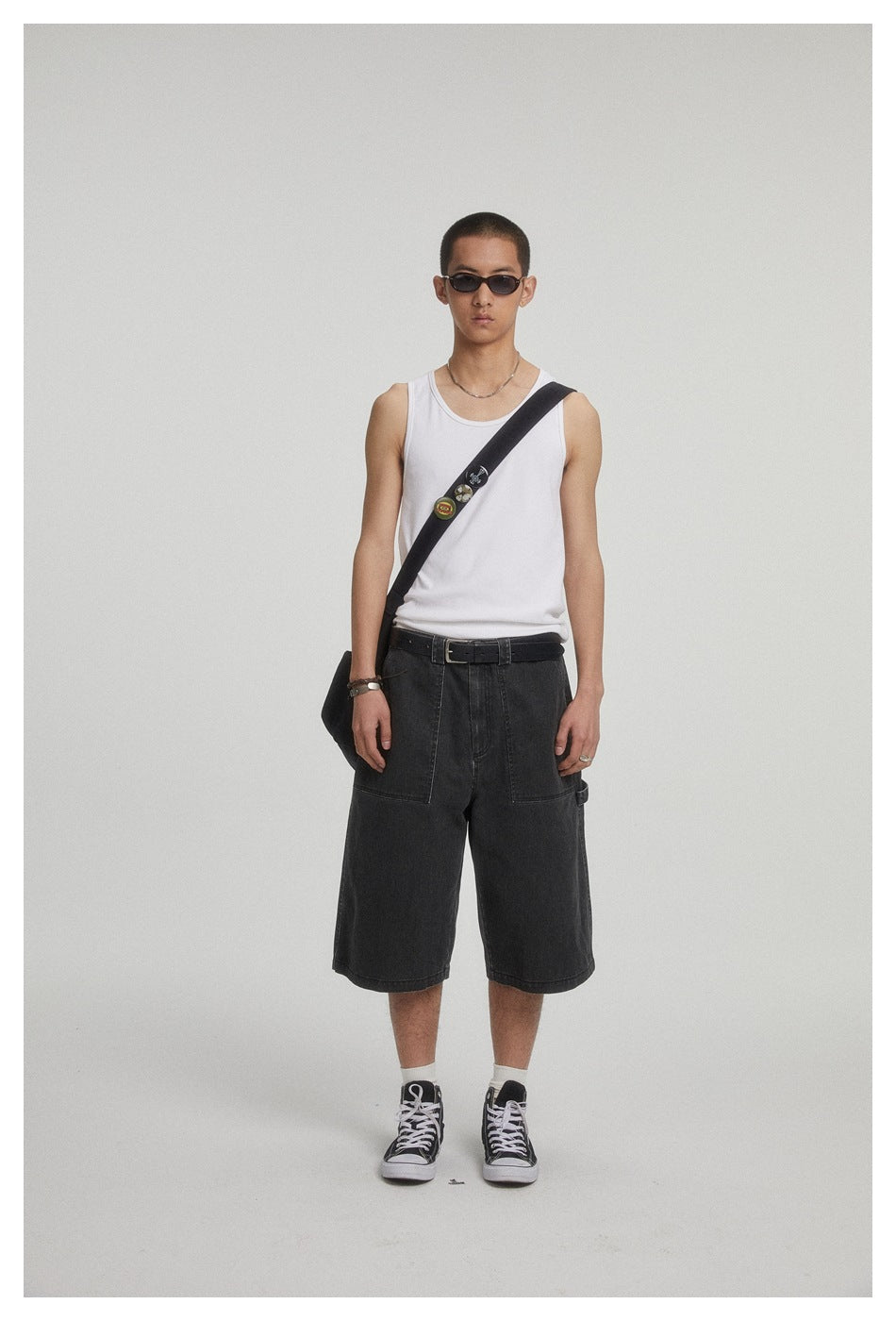 Model wearing black denim knee-length shorts with a white tank top, black belt, crossbody bag and black sneakers