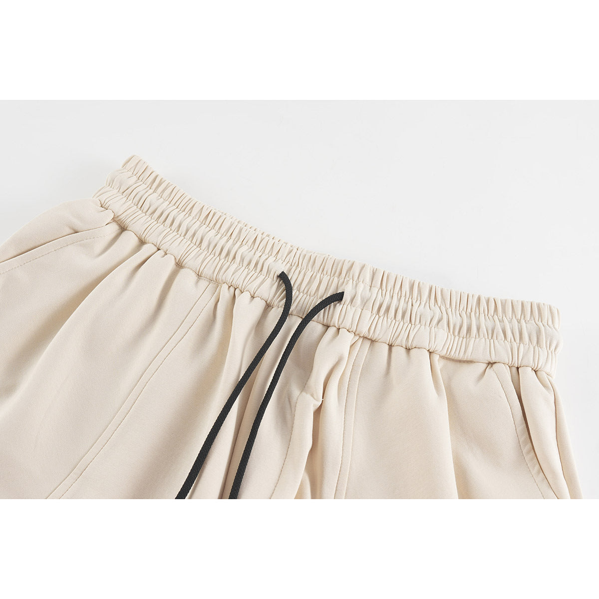 Close-up of cream shorts showing the gathered elastic waistband, black drawcords, and curved pocket seams.