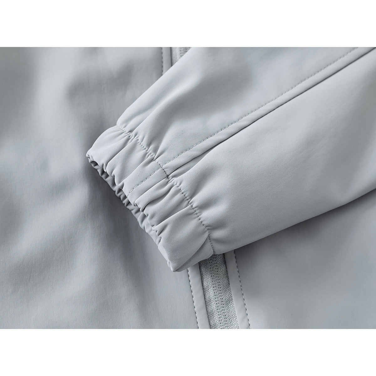 Close-up of a light gray jacket sleeve with an elastic cuff and stitched seam beside the zipper.