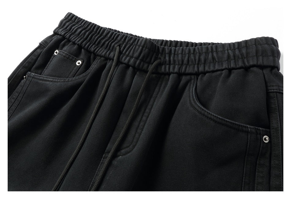 Cropped front view of black pants with an elastic drawstring waist, pleats, front pockets and metal rivets.