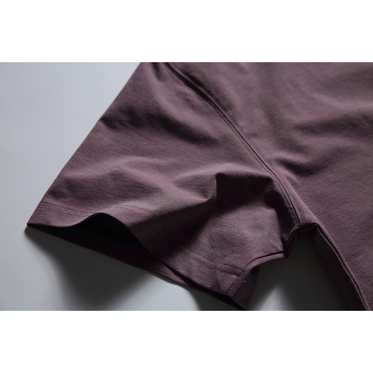 Close-up of the dark plum T-shirt sleeve, hem stitching and underarm seam.