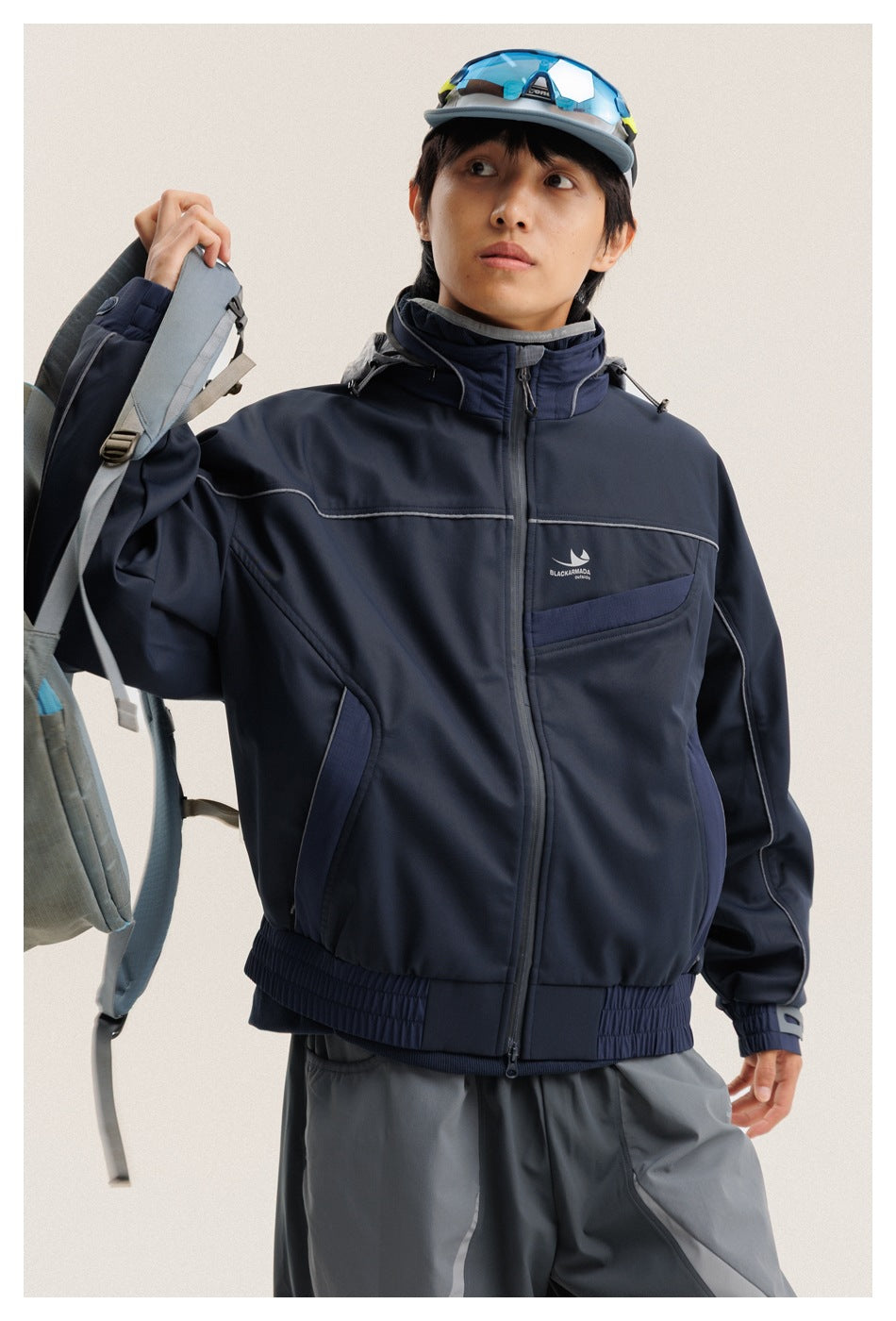Close view of a model in a navy hooded jacket with a zip front, chest pocket, and contrasting piping.