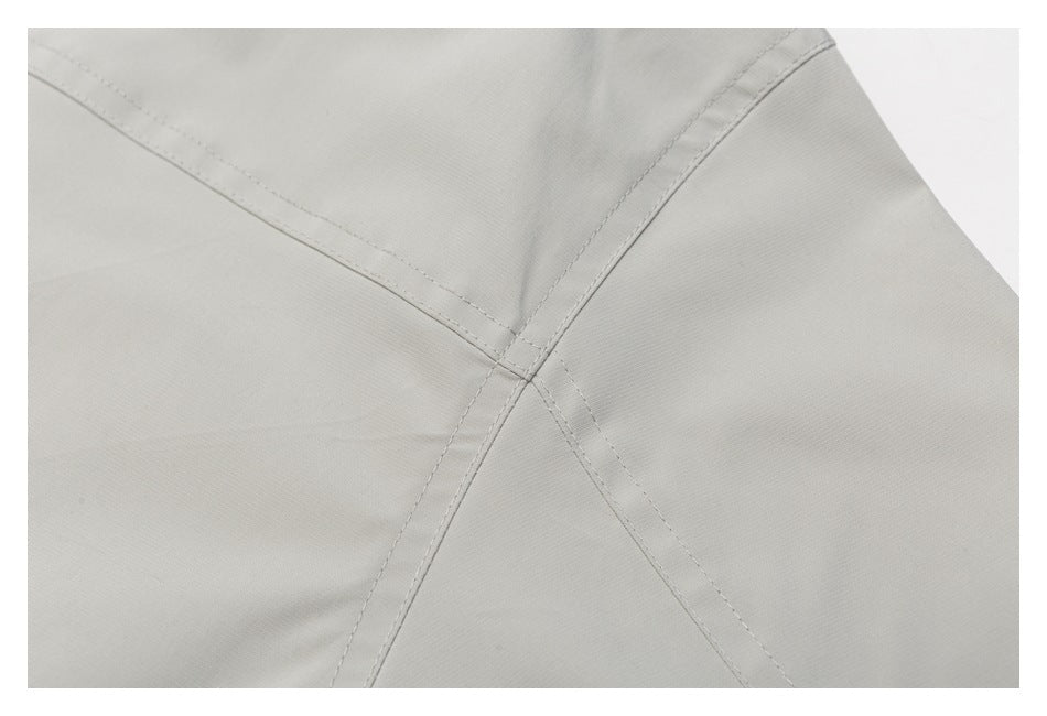 Close-up of intersecting stitched seams on light gray garment fabric.