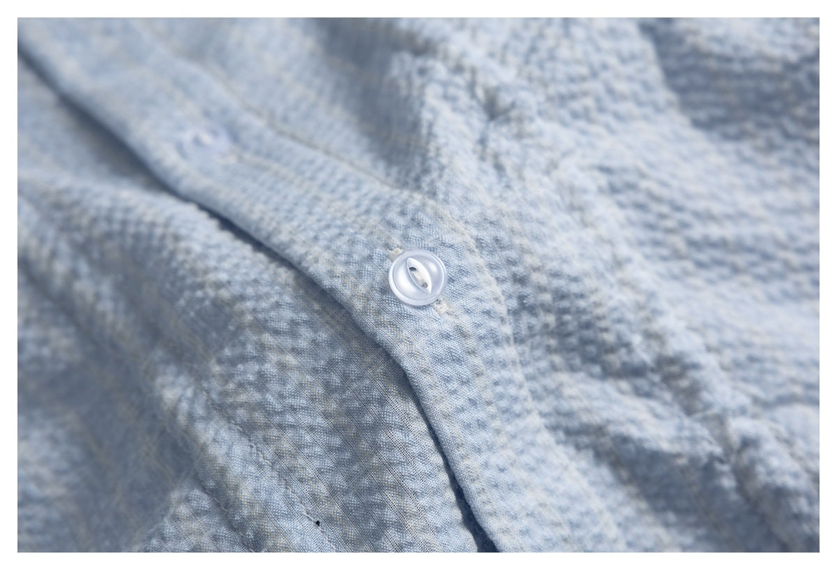 Close-up of a white button and placket on pale blue textured shirt fabric.