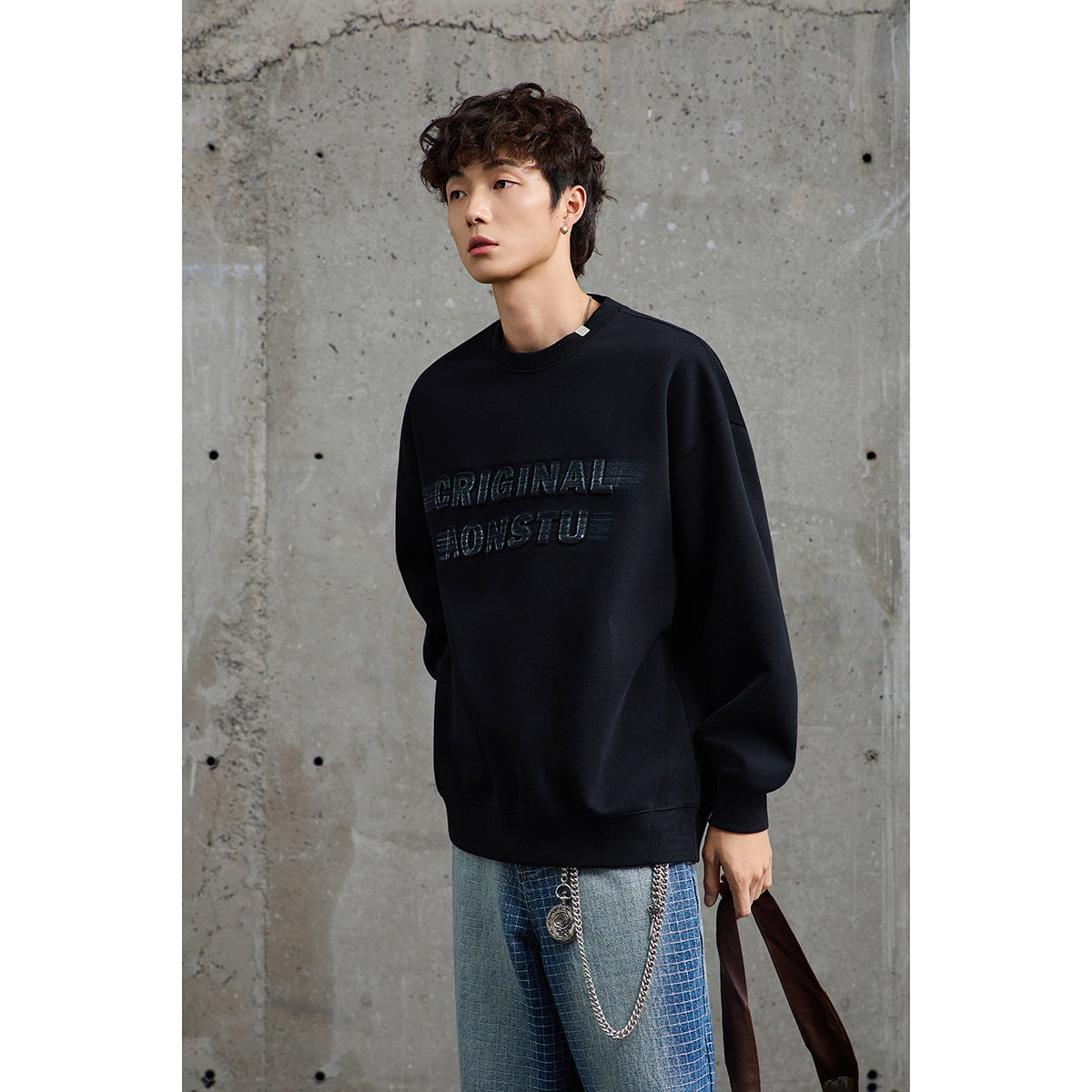 Model wearing an oversized black crewneck sweatshirt with raised lettering and blue plaid wide-leg trousers.