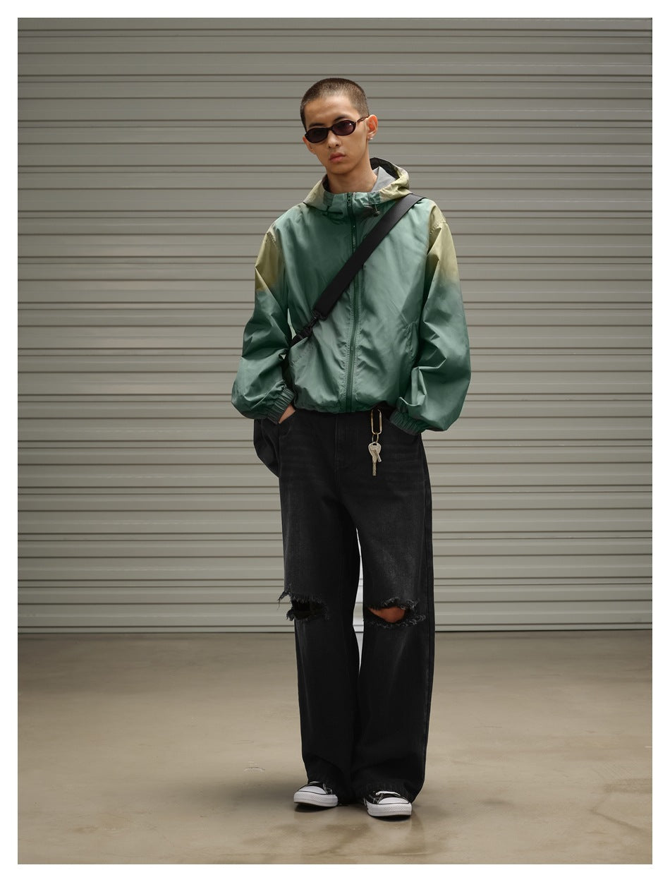 Model wears a sage green hooded zip jacket with olive shoulder accents, black ripped jeans and a crossbody bag.